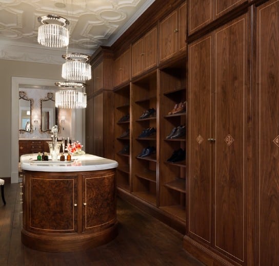 Fine walk-in wardrobe with walnut cabinetry, shoe display, and marble island in Clive Christian’s Chicago showroom